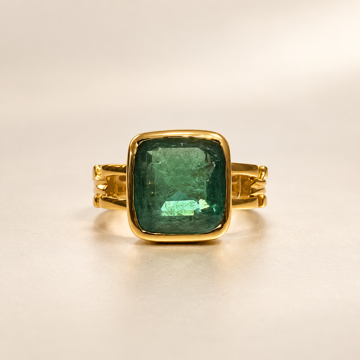 Zambian emerald set in a polished gold ring on a warm ivory studio background